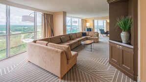 A spacious living room with a large sectional sofa, a round coffee table, and a view of a cityscape through large windows. - Hilton Memphis (Memphis)