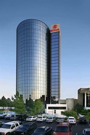 A modern hotel with a cylindrical glass facade and a visible Hilton logo.