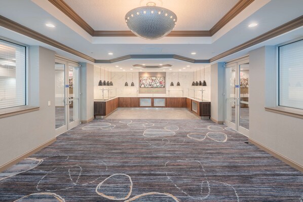 Un hall de hotel con alfombra estampada, una gran lámpara de araña y puertas de cristal que dan a las habitaciones.