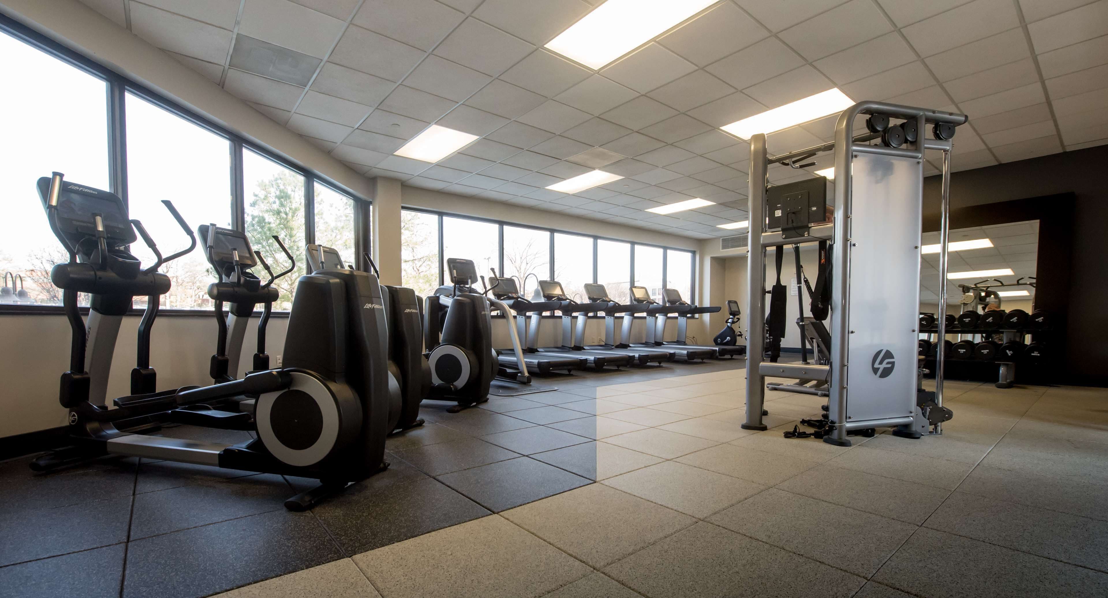 A gym with multiple treadmills, elliptical machines, and a weightlifting area.