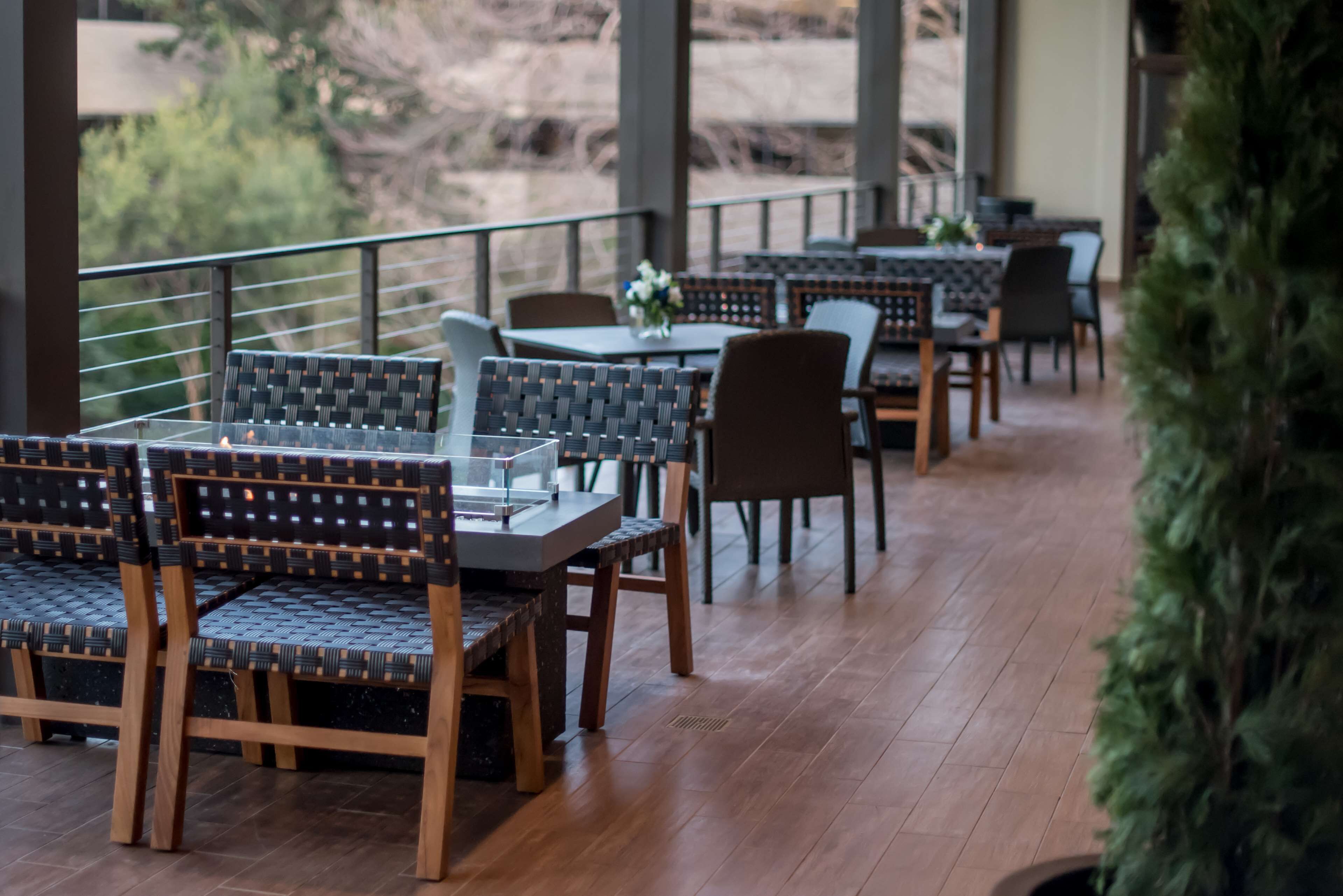A restaurant with outdoor seating, wooden tables, and chairs with woven backs.