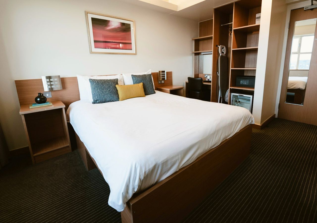 Una habitación de hotel con una cama grande, mesitas de noche, un escritorio y un armario.
