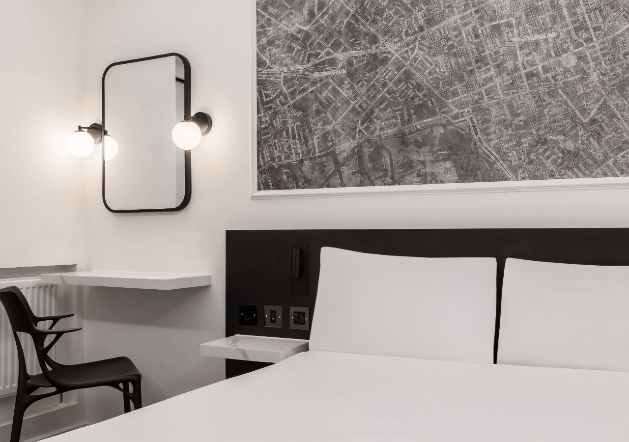 Ein modernes Hotelzimmer mit einem großen Bett, einem Schreibtisch mit Stuhl, einem wandmontierten Spiegel und einer Stadtkarte.