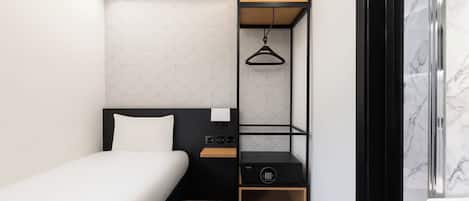 A compact hotel room with a bed, a small bedside table, a wardrobe with hanging space, and a shower area.
