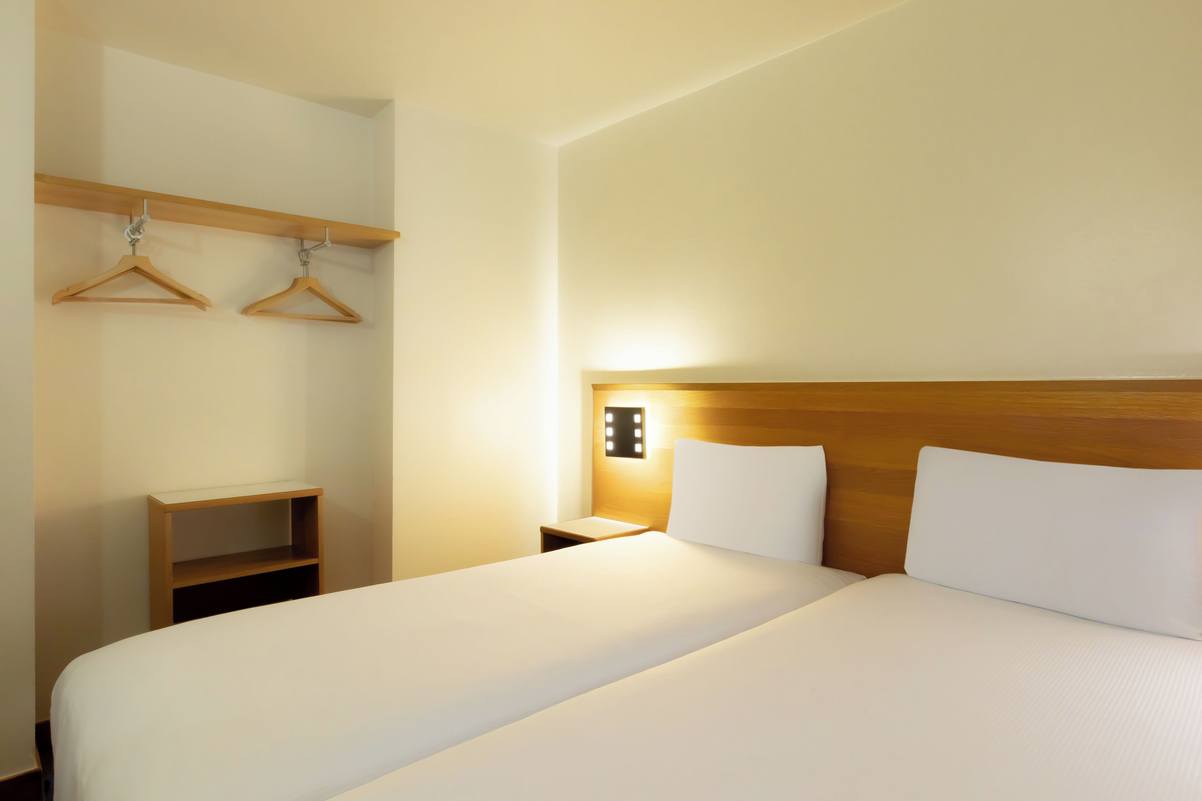 Habitación de hotel con una cama grande, cabecero de madera, mesita de noche y lámpara de pared.