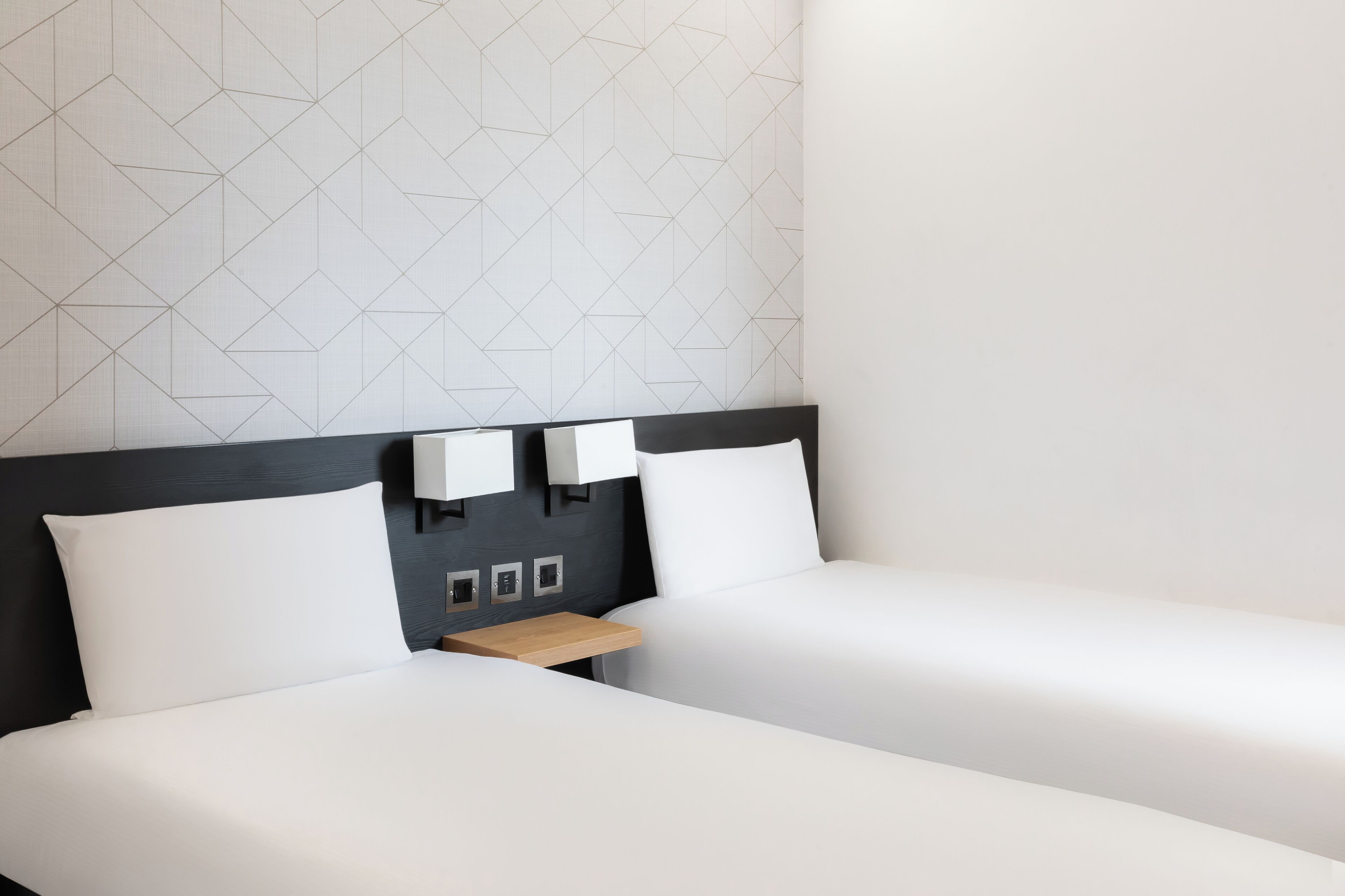 A hotel room with two beds, a wooden nightstand, and a geometric-patterned wall.