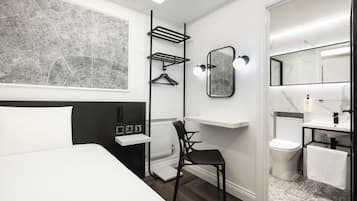 Ein modernes Hotelzimmer mit einem Bett, einem Schreibtisch, einem Stuhl, einem Badezimmer mit Toilette und Waschbecken sowie einer großen Karte an der Wand.