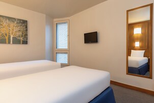 A hotel room with two beds, a TV, a painting, and a large mirror.