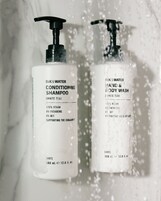 Dos botellas de champú y gel de baño con dosificador tipo bomba, ambas etiquetadas como 100% veganas y que apoyan a la comunidad.