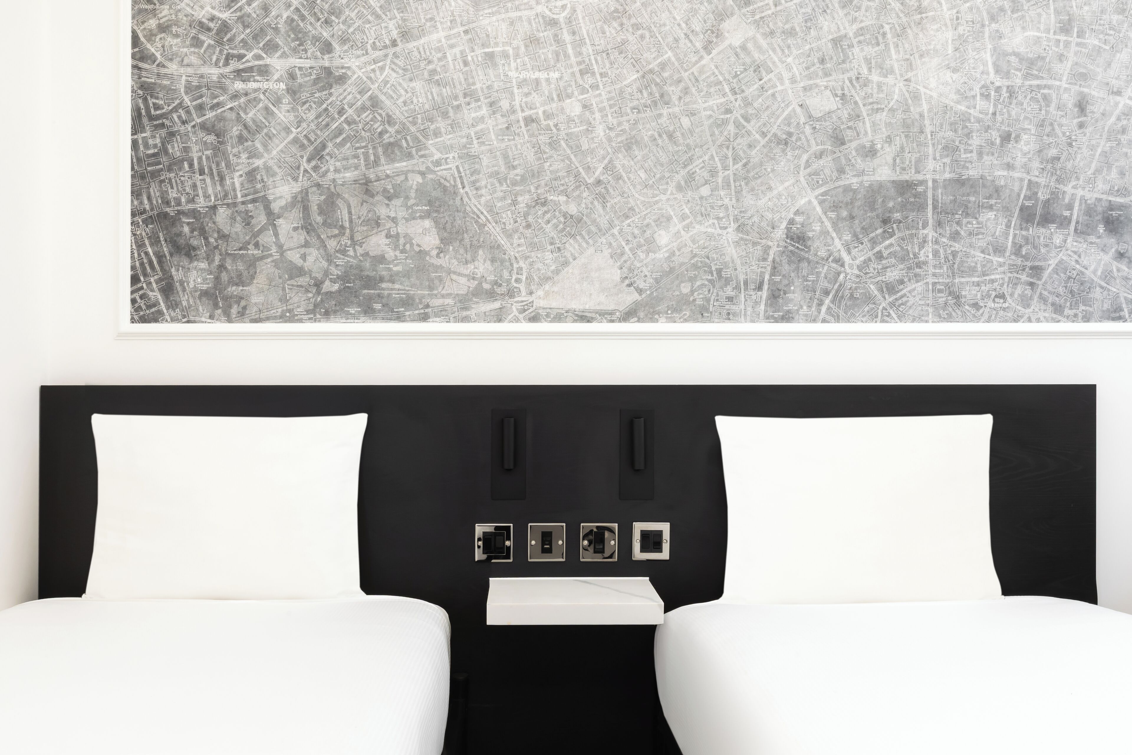 A hotel room with a black headboard, two white beds, a map on the wall, and a flat-screen TV.