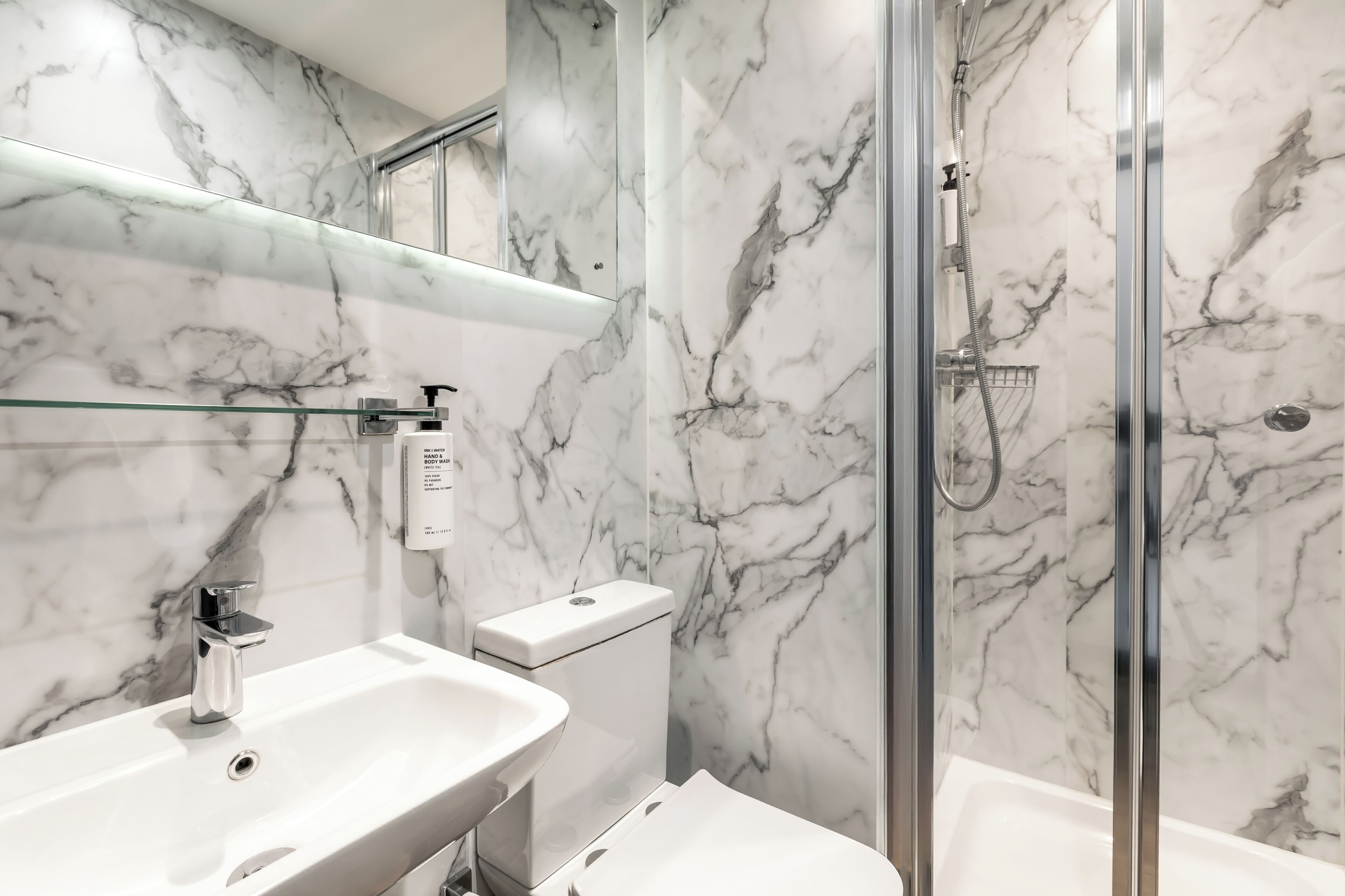A bathroom with a marble wall, a glass shower enclosure, a sink, and a toilet.