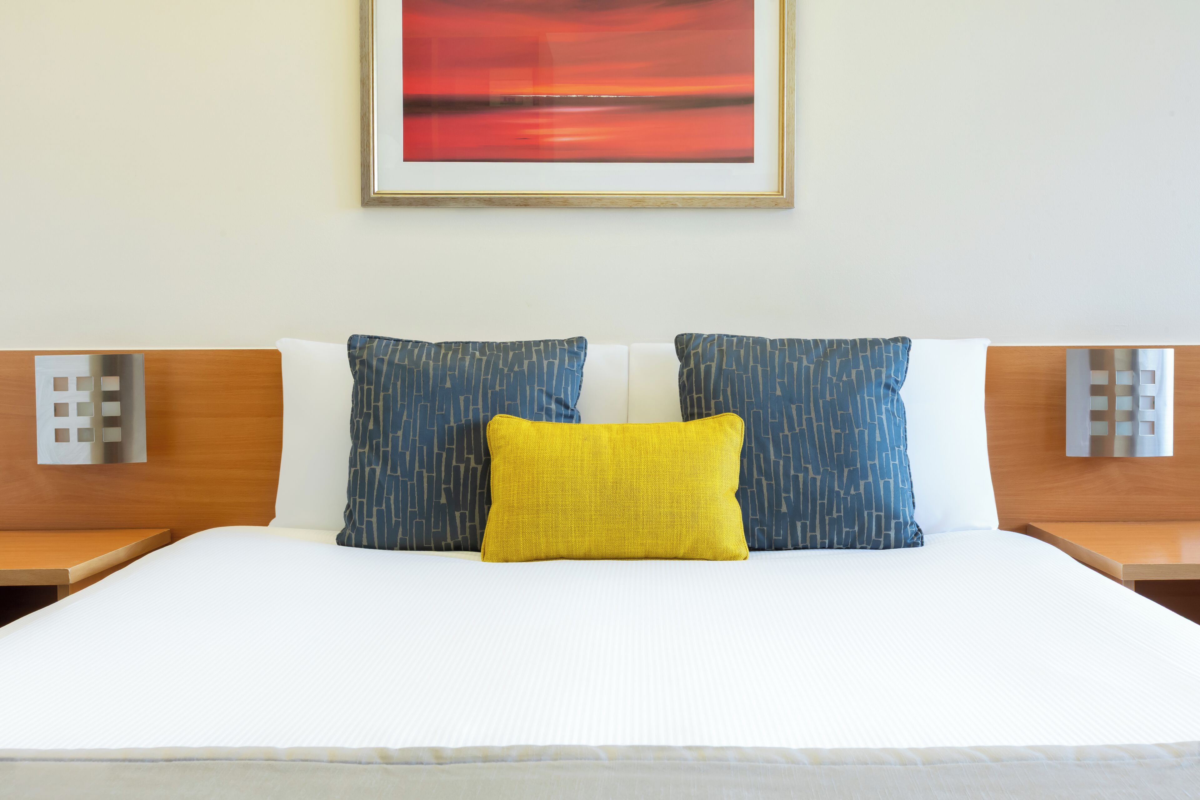 A hotel room with a bed, two nightstands, a wall-mounted light, and a framed picture.