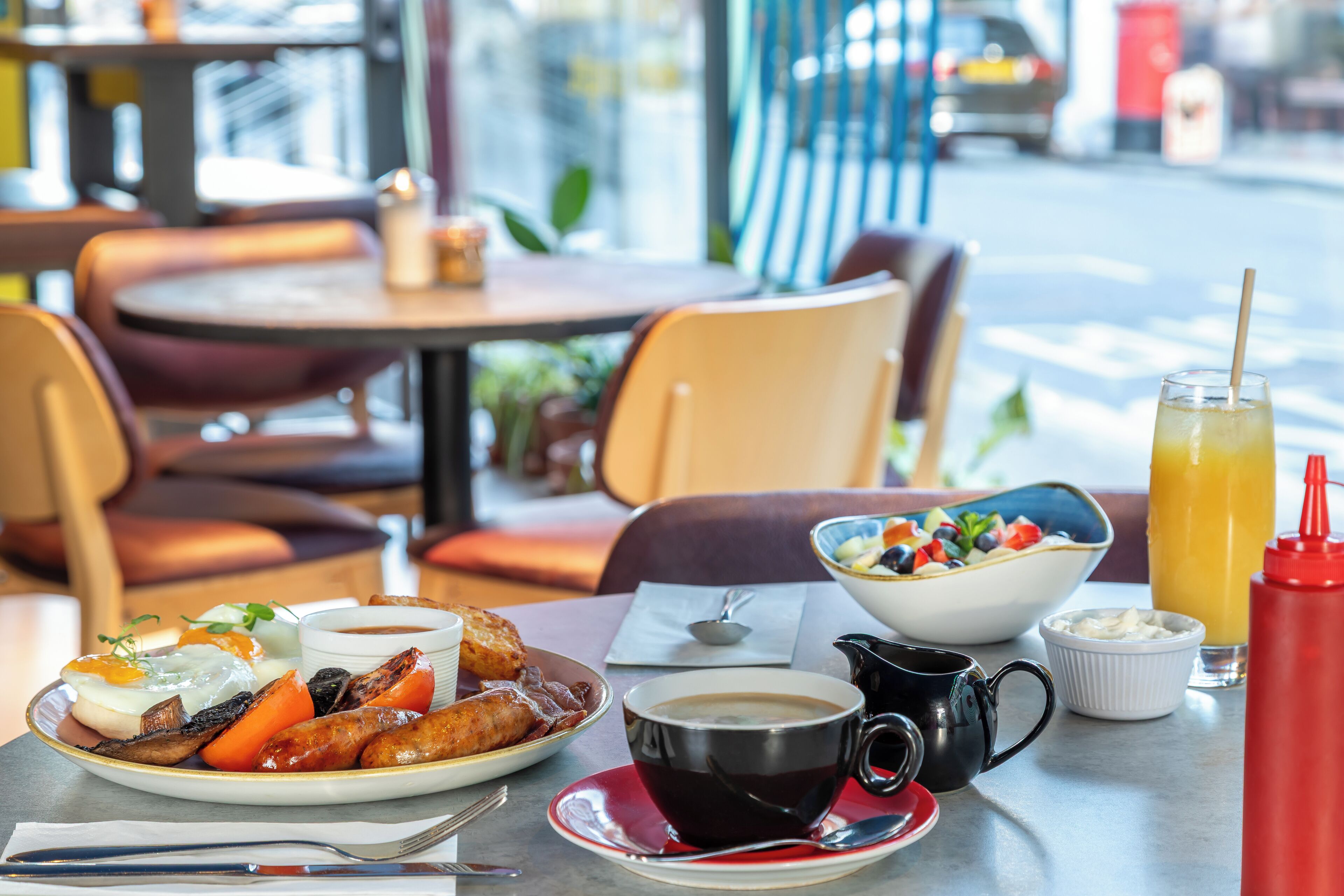 A breakfast setting with a plate of food, a coffee cup, a bowl of fruit, and a glass of orange juice.