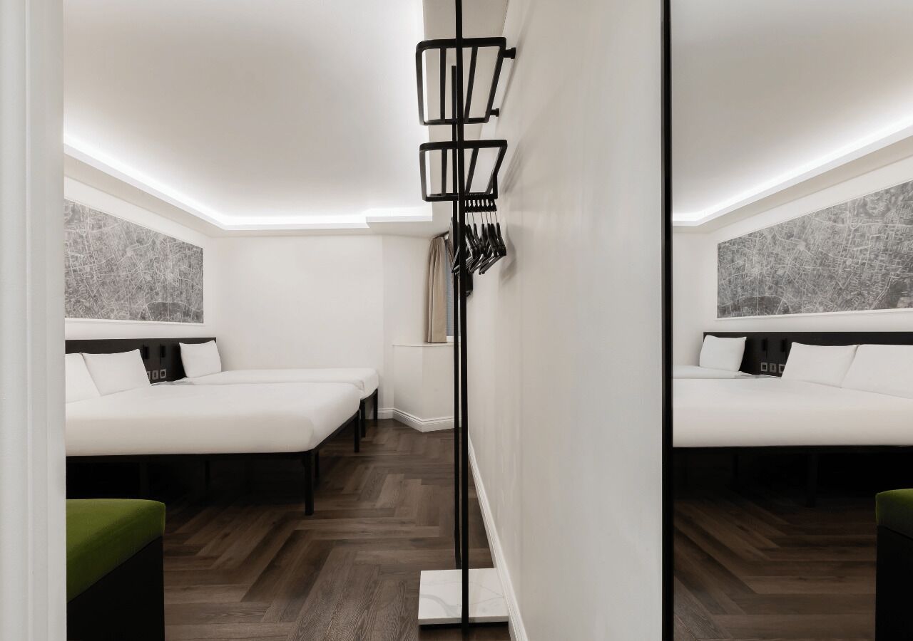 A modern hotel room with two beds, a floor lamp, and a cityscape view.