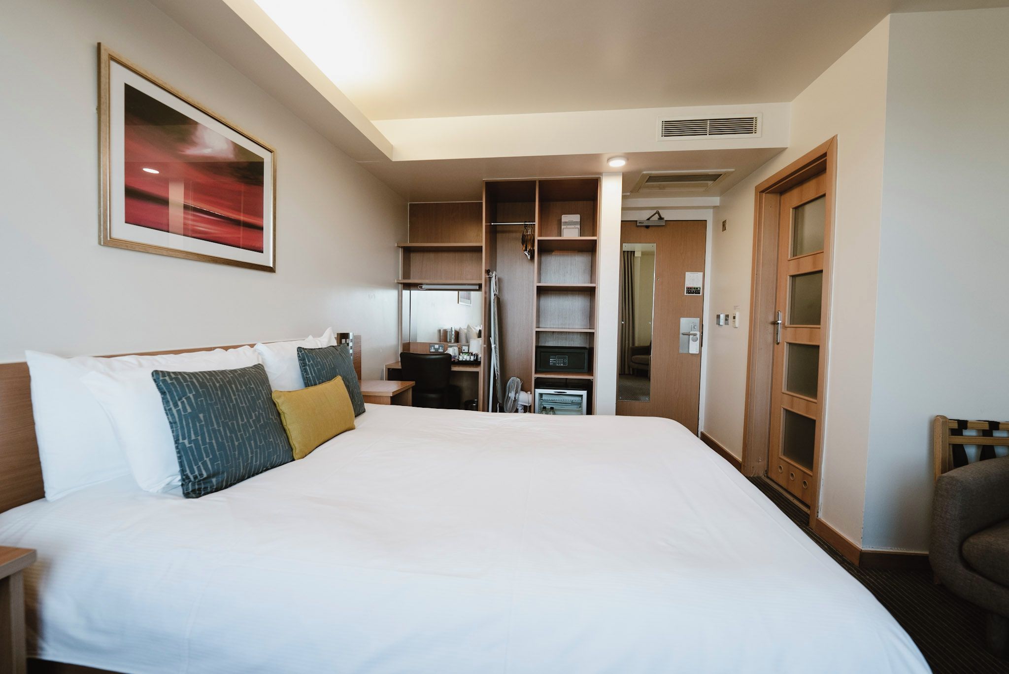A hotel room with a large bed, a desk, a wardrobe, and a bathroom visible through an open door.