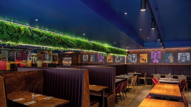 A restaurant with booths and tables, green plants on the ceiling, and framed pictures on the walls. -  STG Hotel London Oxford Street (London)
