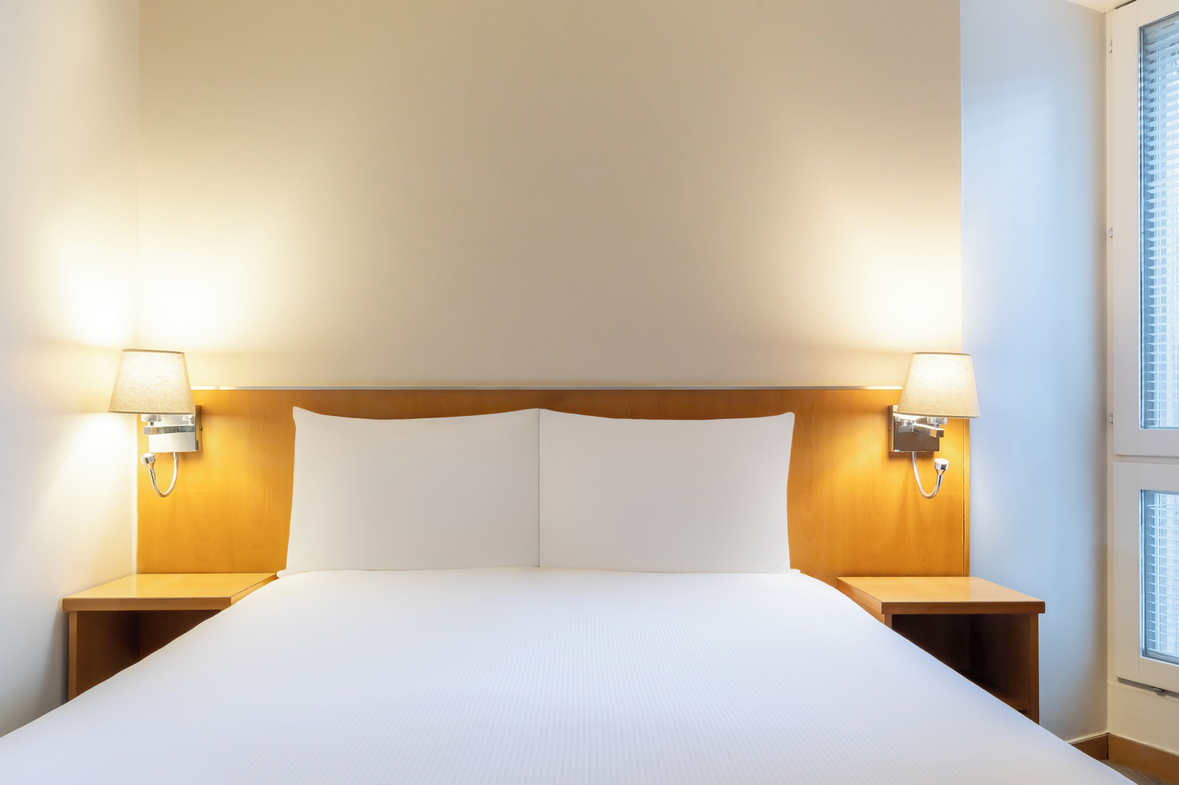 Habitación de hotel con una cama grande, dos lámparas de noche y una ventana con persianas.