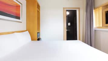 Ein Hotelzimmer mit einem großen Bett, einem gerahmten Bild an der Wand, einem Holzregal und einer Tür zu einem Badezimmer.