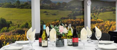 Une table à manger dressée avec de l’argenterie blanche, des verres et des couverts, bordée de bouteilles de vin et agrémentée d’un vase rempli de fleurs.