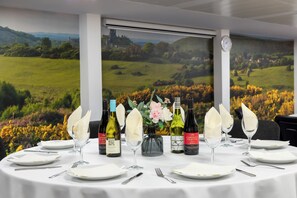A dining table set with white plates, glasses, and cutlery, flanked by wine bottles and a vase with flowers. -  STG Hotel London Oxford Street (London)