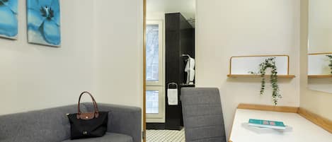 A modern hotel room with a grey sofa, a small desk, and a bathroom visible through an open door.