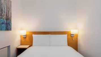 A hotel room with a wooden headboard, two bedside lamps, a white bed, and a painting on the wall.