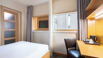 Habitación de hotel con cama, escritorio con silla, cafetera y ventana con persianas.