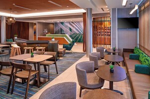 Un moderno vestíbulo de hotel con una recepción, zonas de estar y una pantalla de televisión.