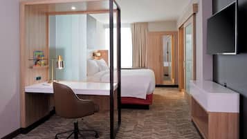 Habitación de hotel con escritorio, silla, cama, televisor y espejo.
