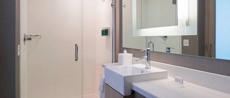 A modern bathroom with a glass-enclosed shower, a white sink, and a large mirror.