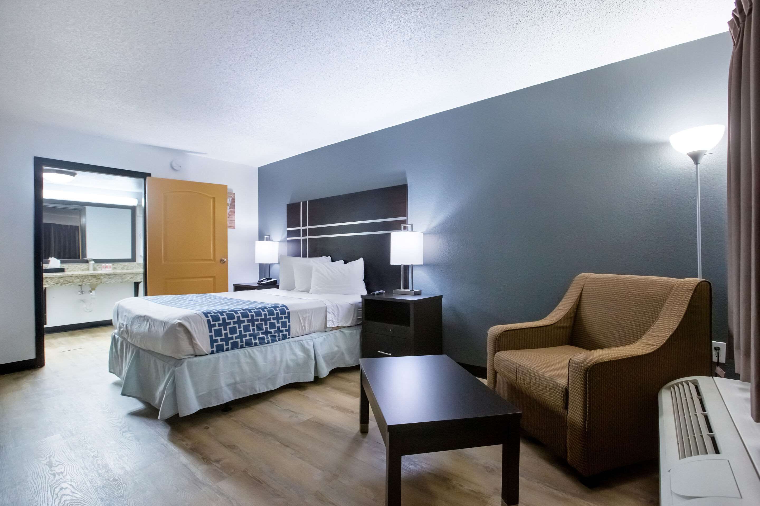 Una habitación de hotel con una cama, mesitas de noche, una silla, una mesa y una lámpara.