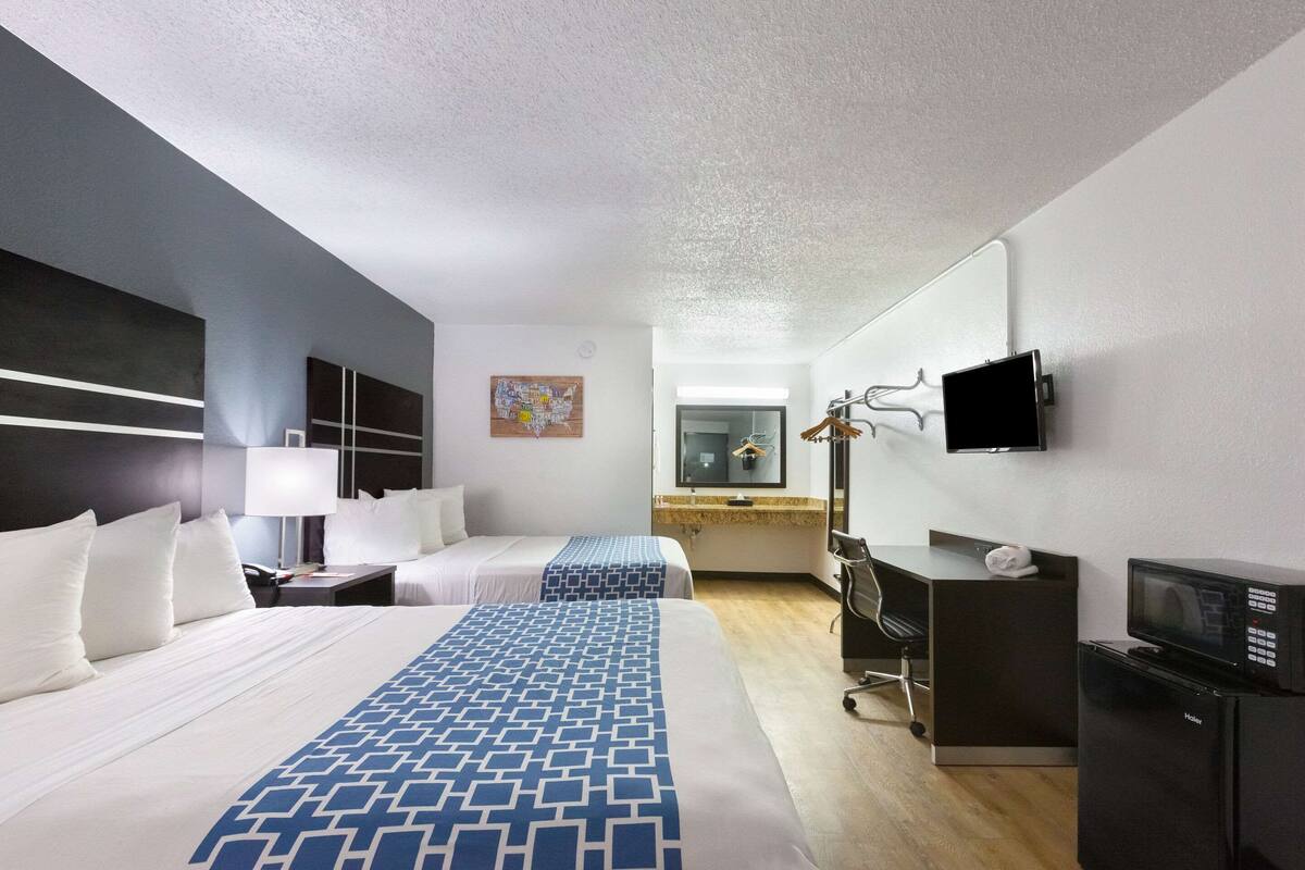 Ein Hotelzimmer mit zwei Betten, einem Schreibtisch, einem Sessel, einem Fernseher und einer Mikrowelle.