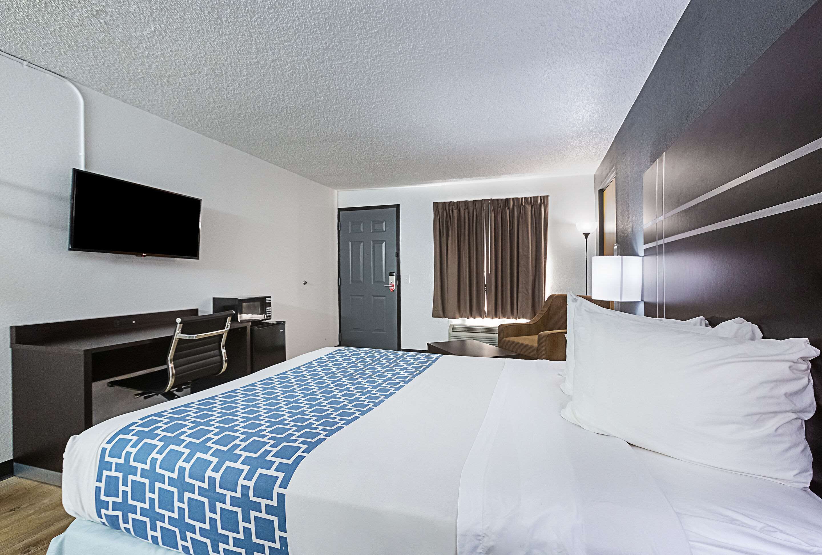 A hotel room with a bed, a desk, a chair, a flat-screen TV, and a door.