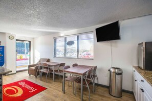 A hotel room with a dining area, a TV mounted on the wall, and a window with blinds.