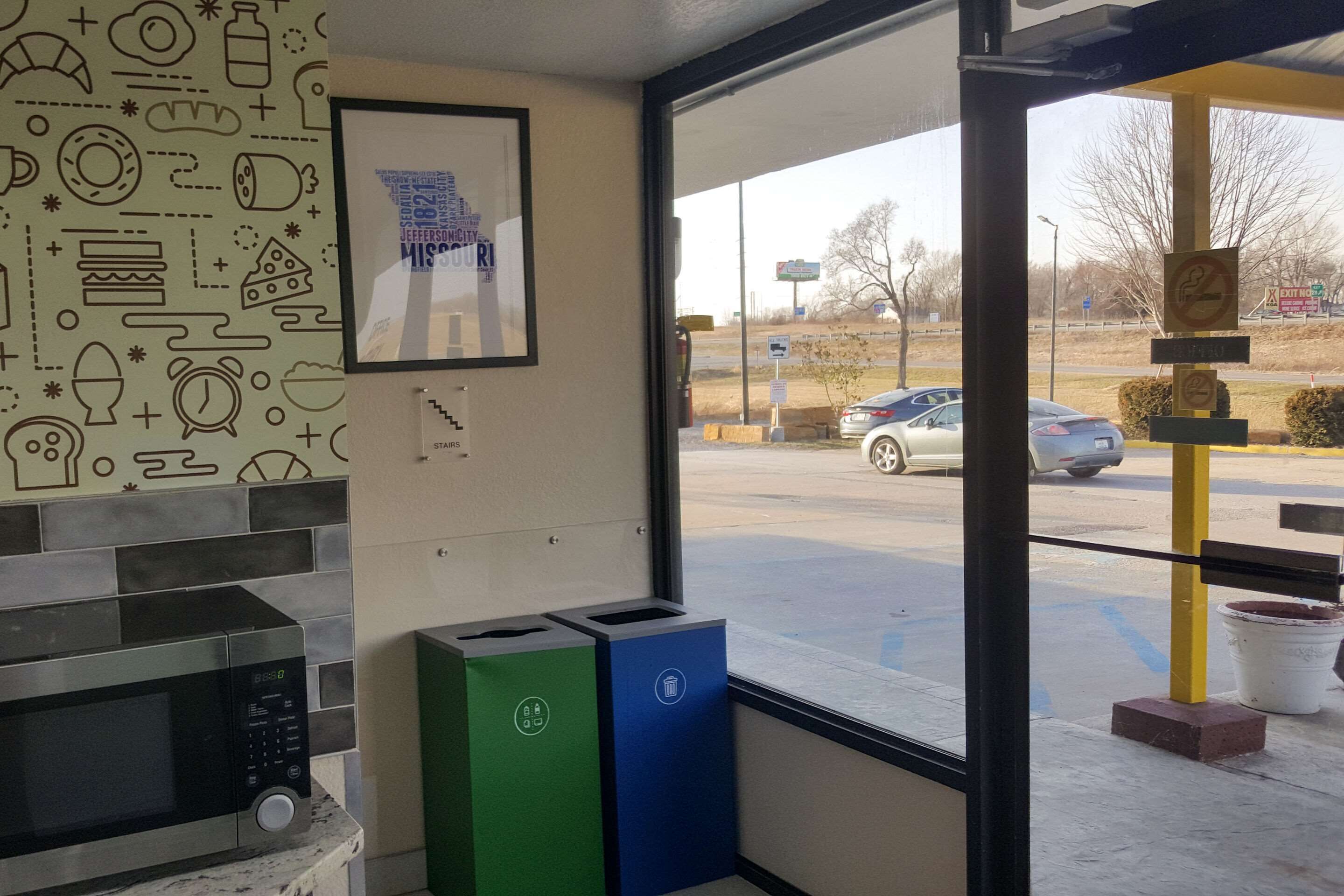Una cucina con un forno a microonde, due cestini e una finestra che dà su un parcheggio e una strada.