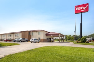 Un Red Roof Inn con estacionamiento, un área de estar al aire libre techada y cielo despejado.