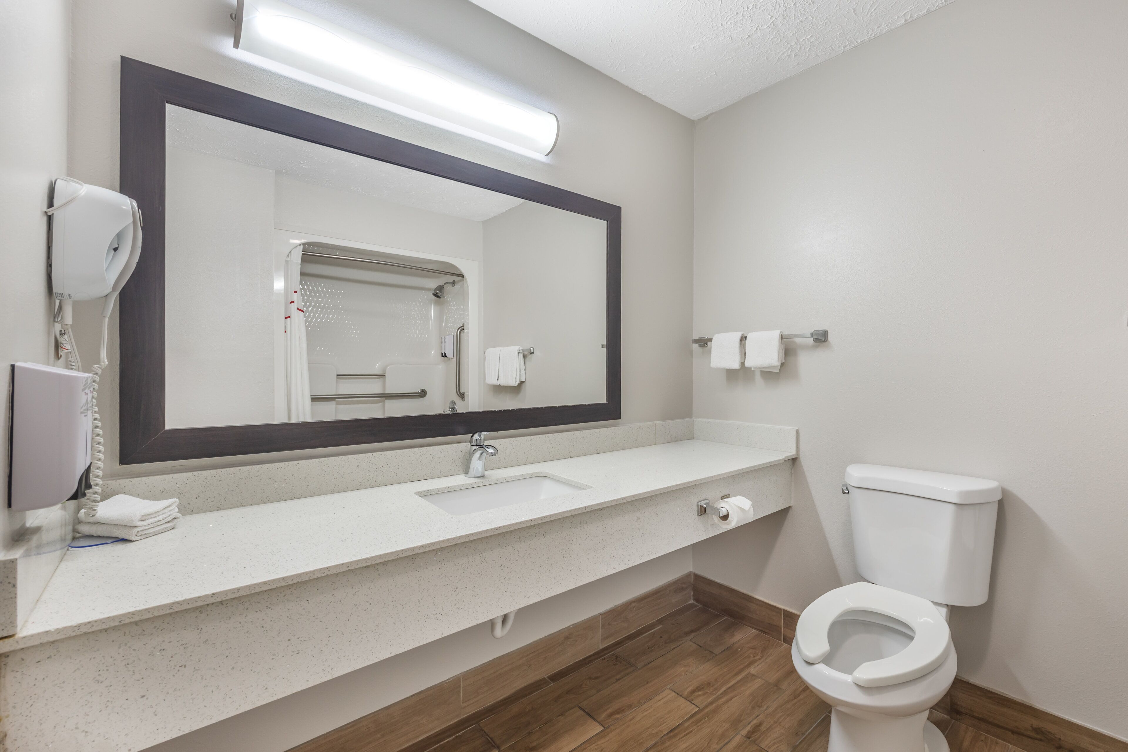 Une salle de bain avec un lavabo blanc, un grand miroir, des toilettes et un sèche-cheveux.