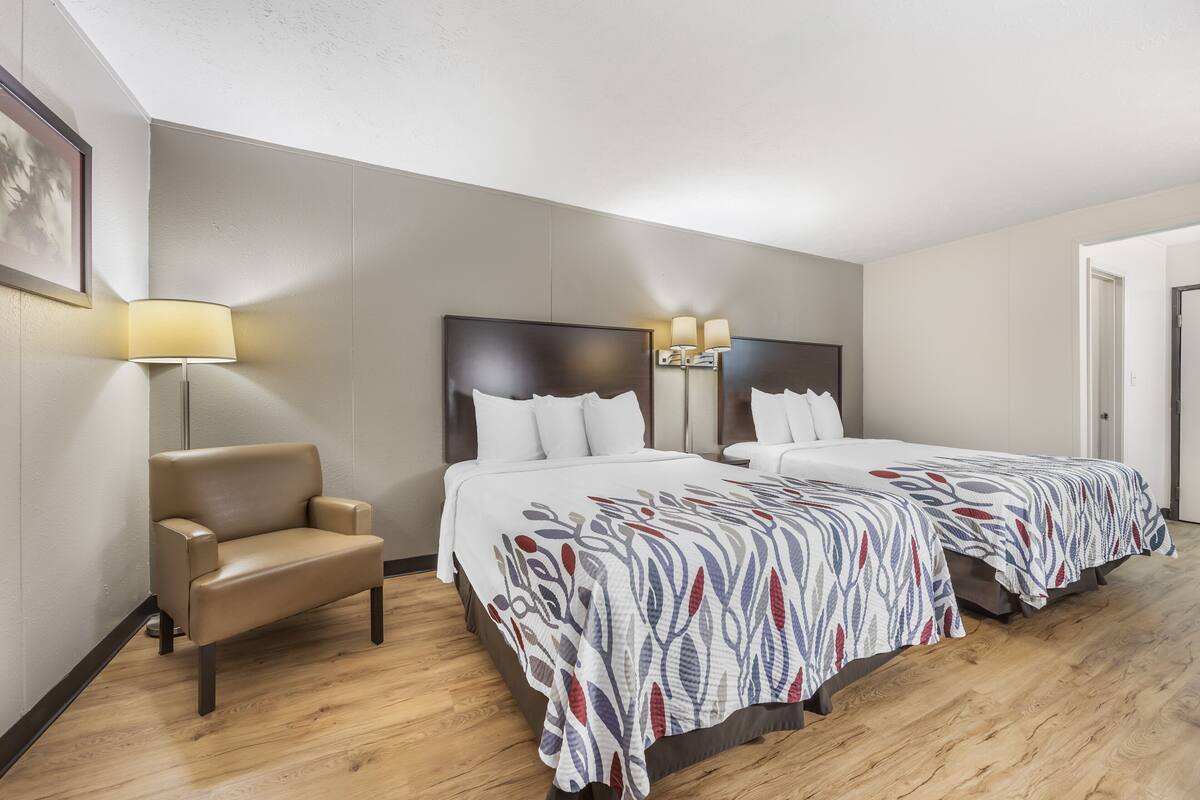 Una habitación de hotel con dos camas, una silla y una lámpara.