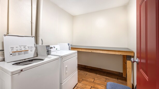 A compact laundry room with a washing machine, a drying rack, and a wooden bench. - Red Roof Inn Paducah (Paducah)