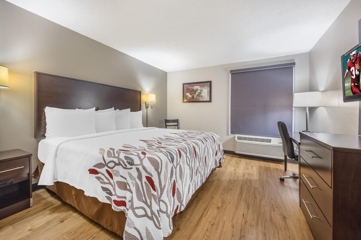Ein Hotelzimmer mit einem großen Bett, einem Schreibtisch, einem Sessel und einem Fernseher.