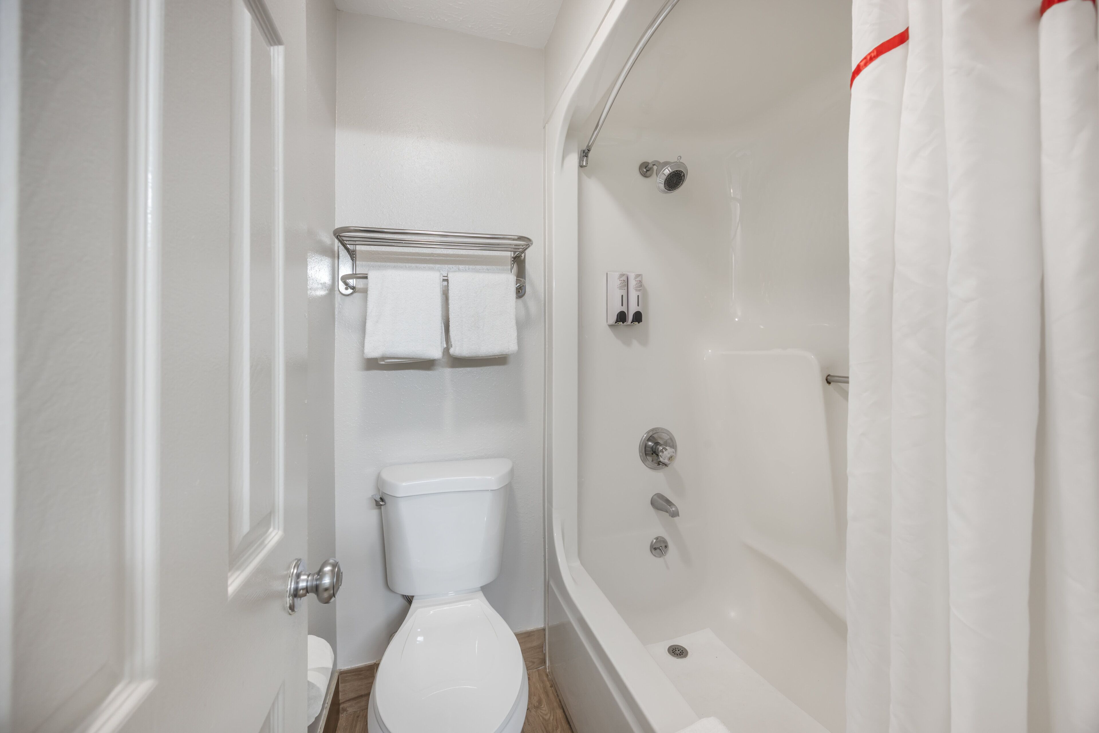 Ein kleines, weißes Badezimmer mit Toilette, Dusche und Handtuchhalter.