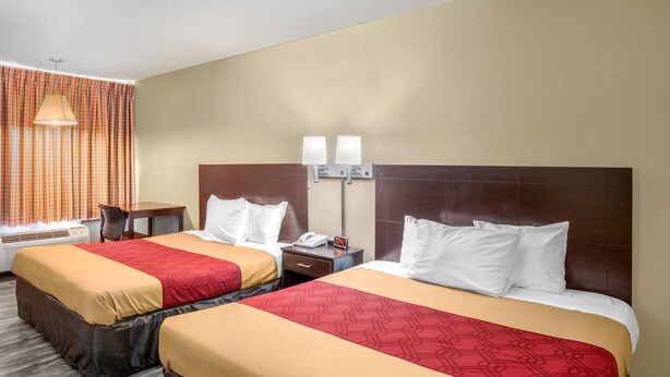Una habitación de hotel con dos camas, un escritorio, una lámpara y una ventana con cortinas.