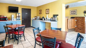 Un comedor con una mesa de madera y sillas rojas, un área de cocina con microondas y cafetera, y una encimera de madera con un reloj.