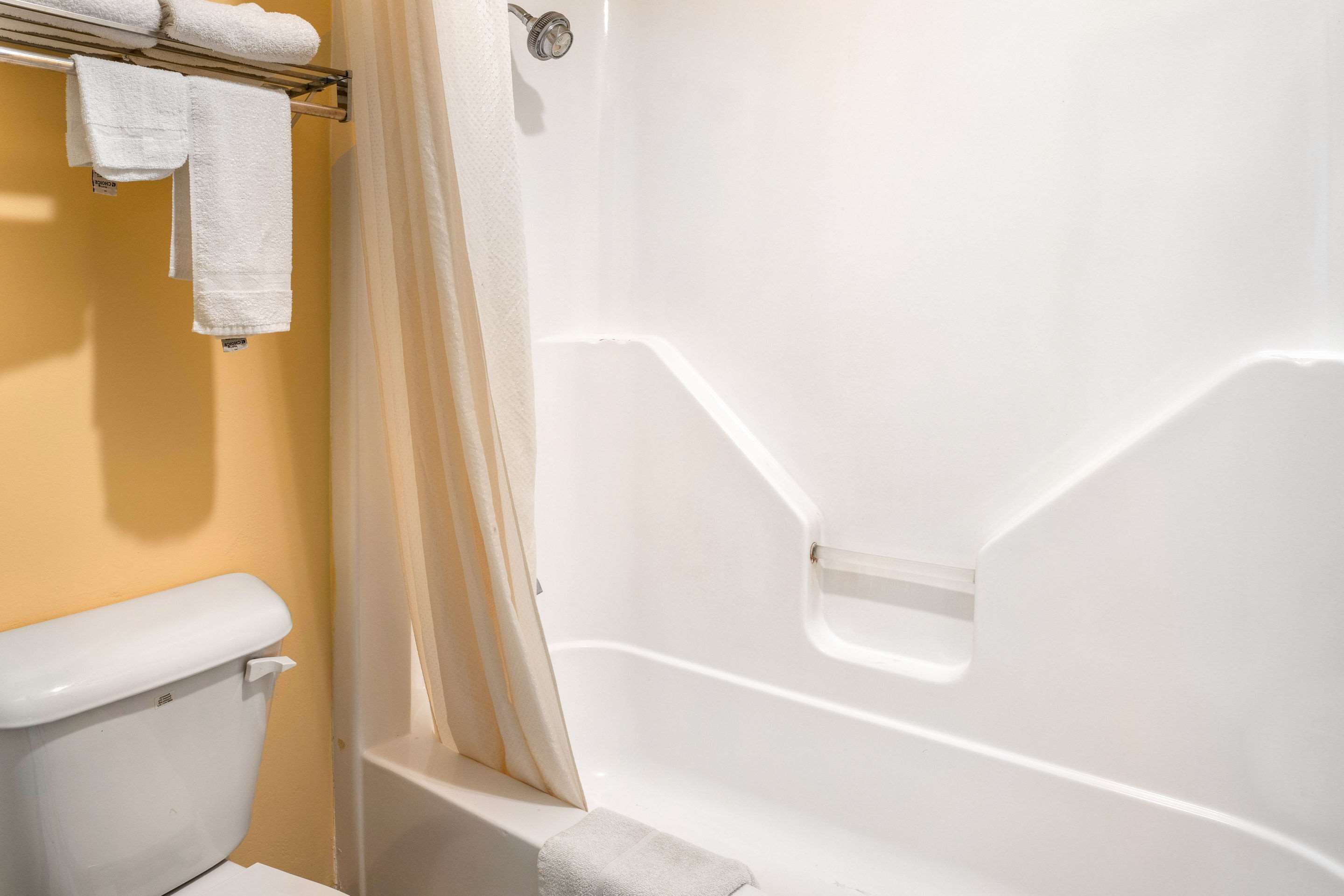 A bathroom with a white bathtub, a toilet, and a towel rack with towels.