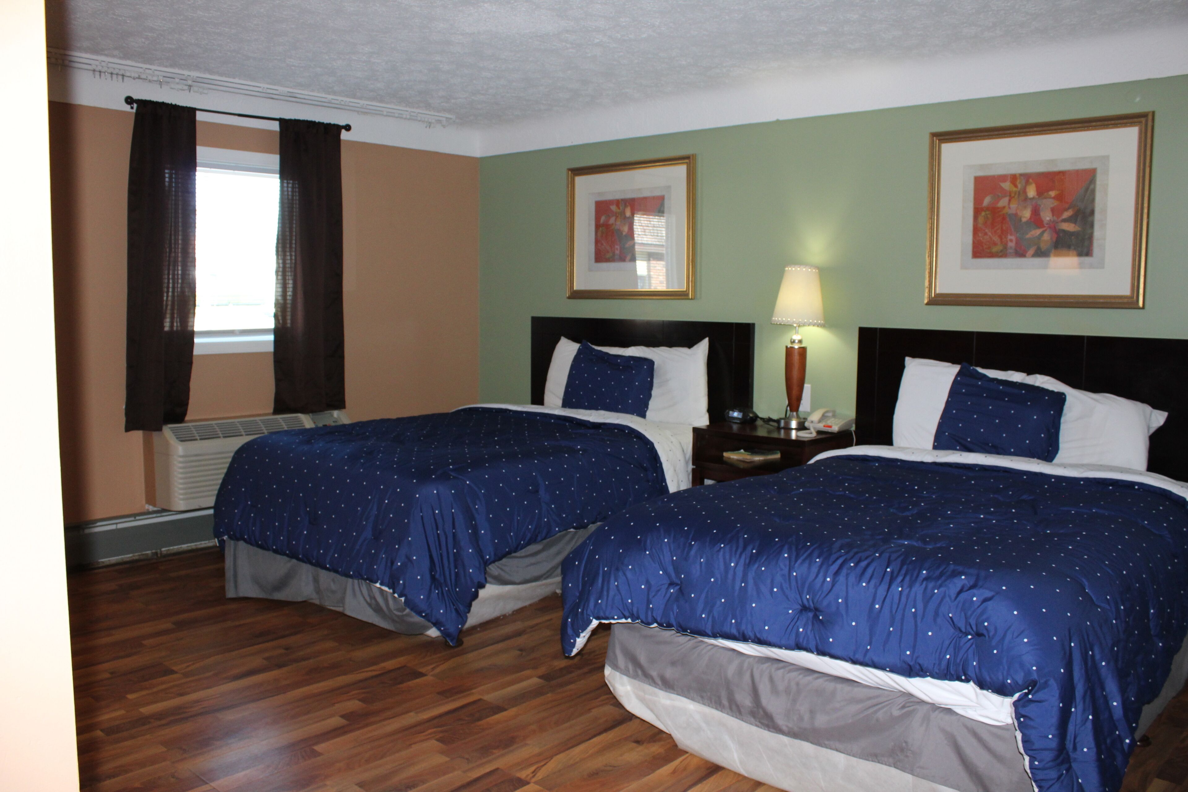 A hotel room with two beds, a nightstand, a lamp, and two framed pictures on the wall.