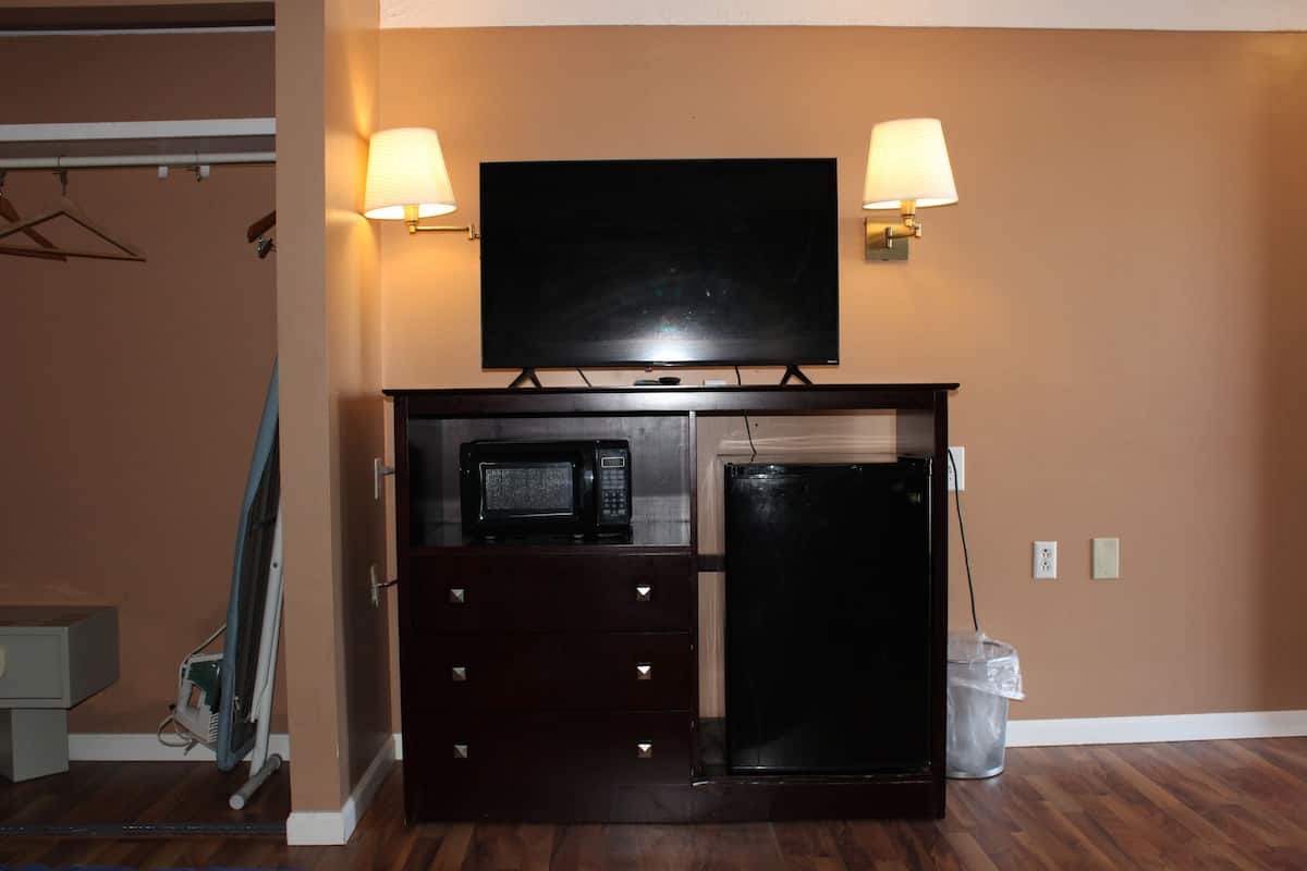 A room with a flat-screen TV mounted above a dark wooden cabinet with a microwave and refrigerator. There are two wall-mounted lamps on either side of the TV.