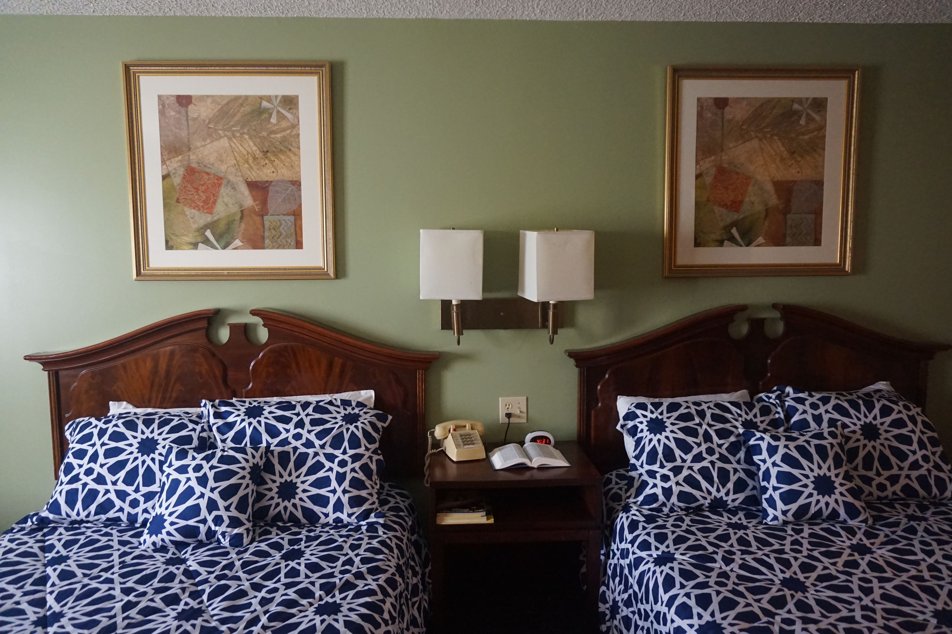 Habitación de hotel con dos camas, cada una con una colcha estampada, una mesita de noche con teléfono y libro, y dos obras de arte enmarcadas en la pared.