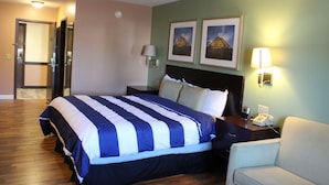 Ein Hotelzimmer mit einem großen Bett, einem Nachttisch mit Lampe, einem Sessel und zwei gerahmten Bildern an der Wand.