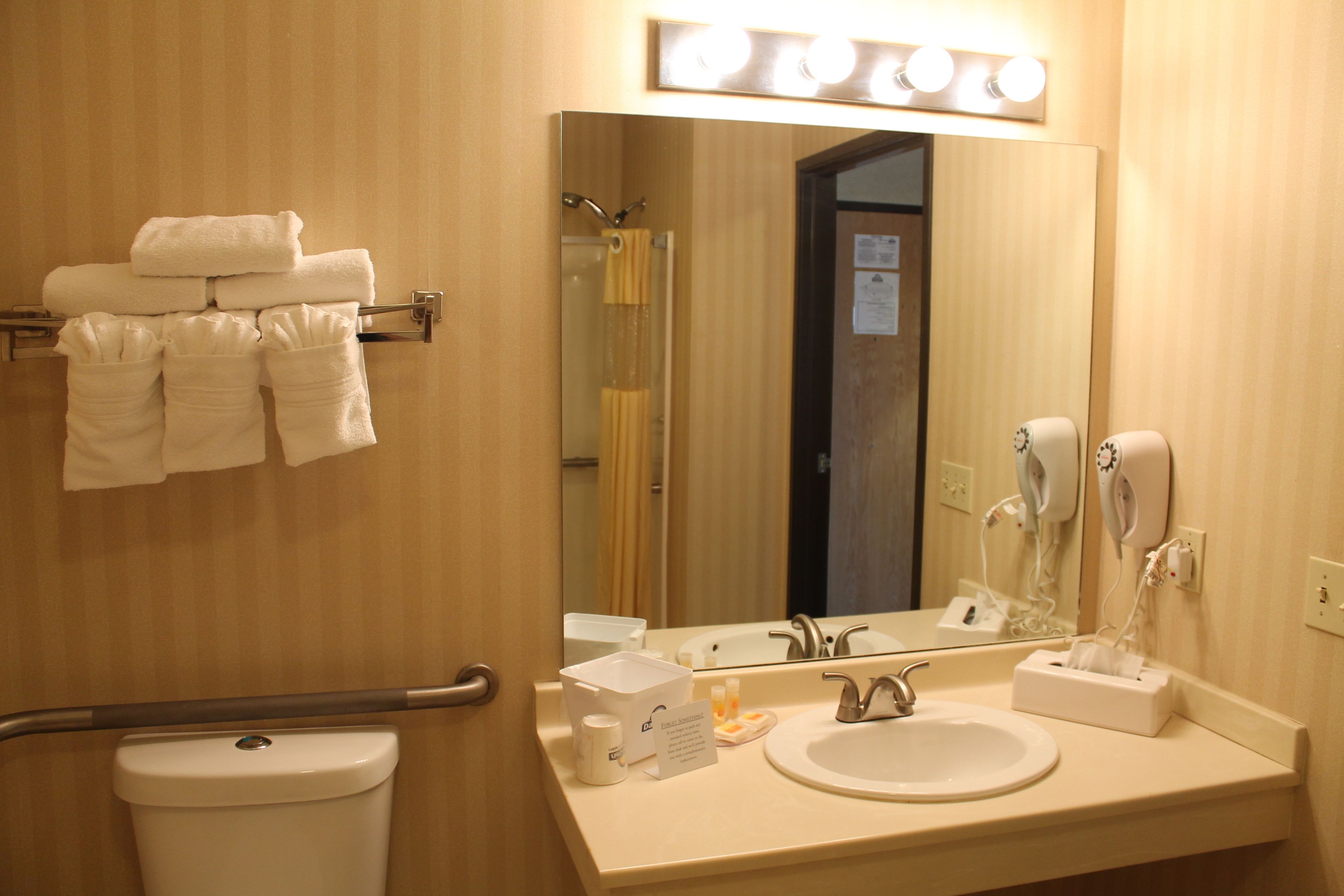 A hotel bathroom with a toilet, sink, hand dryer, and towel rack.