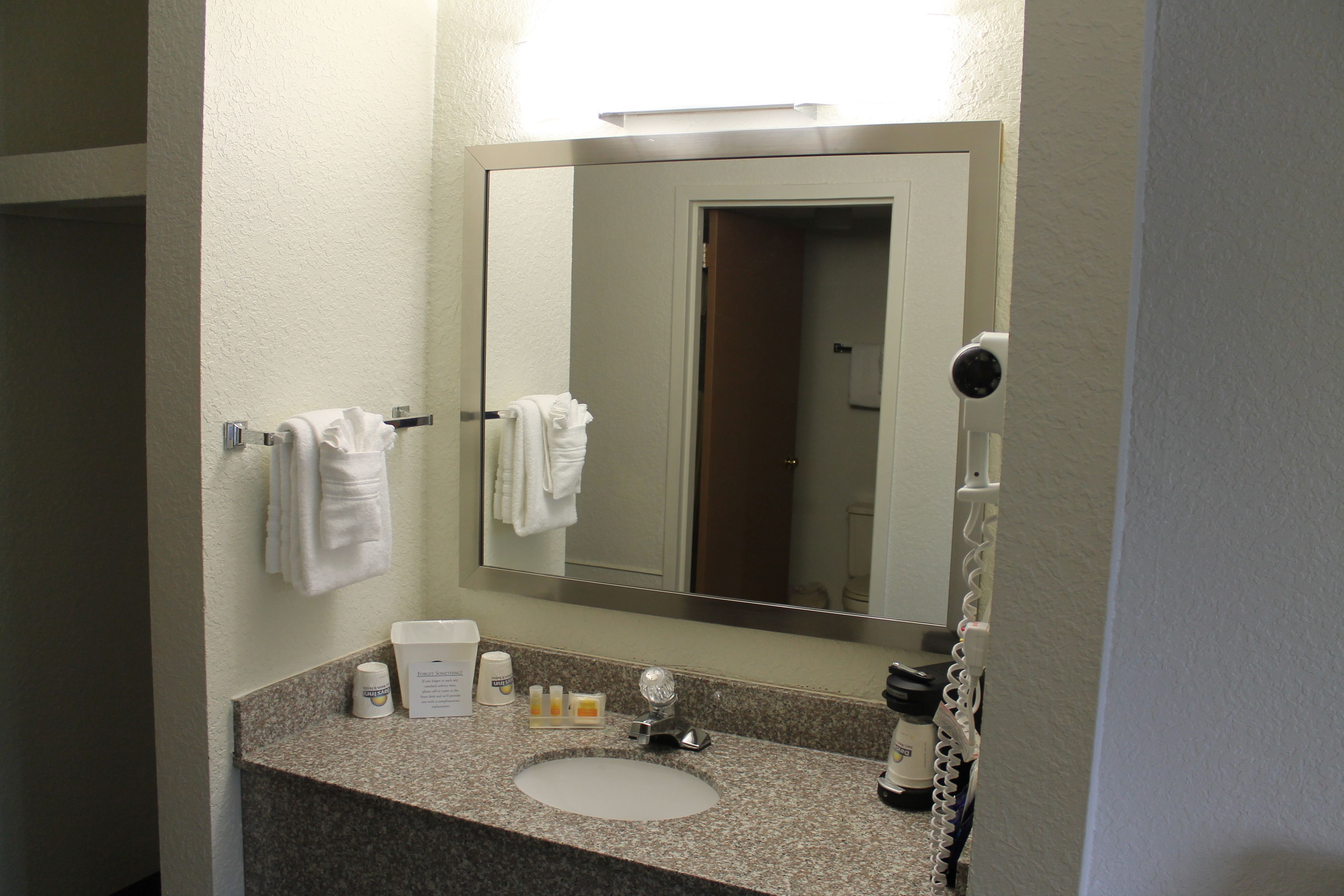 A bathroom with a granite countertop, a white sink, a mirror, and a towel rack with folded towels.
